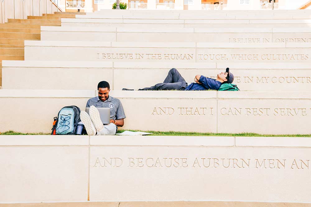 Students sit outside on steps featuring the Auburn Creed