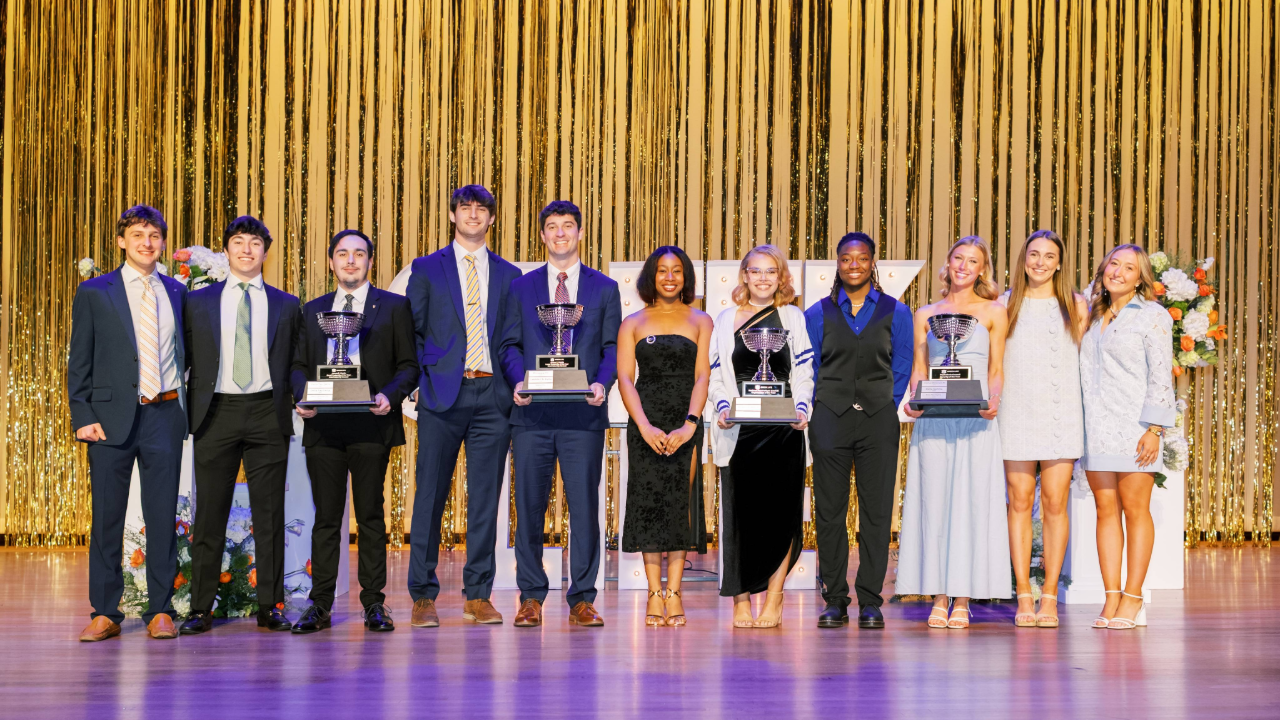 Students standing on stage with large trophies