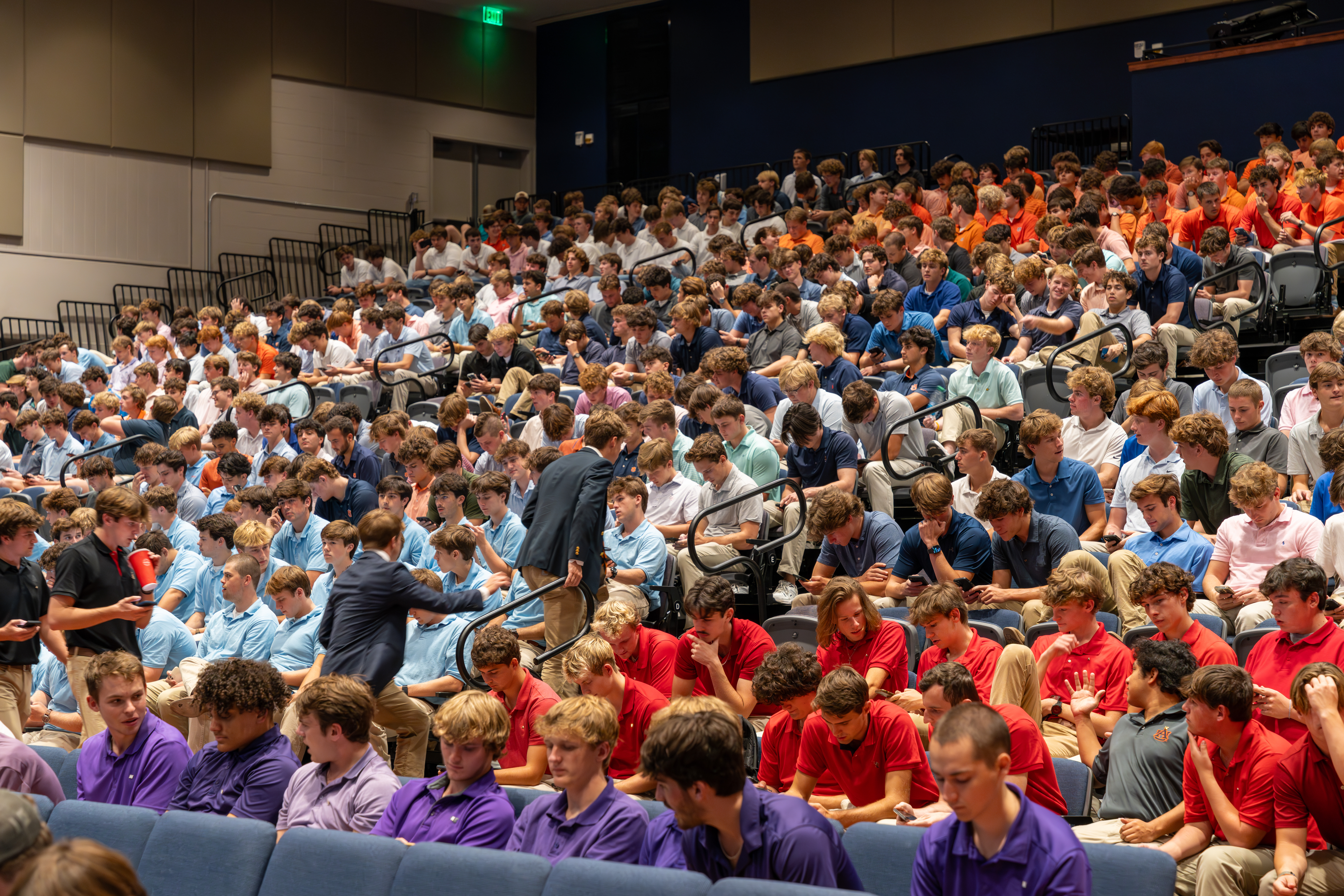 Large group of men sitting on auditorium risers.