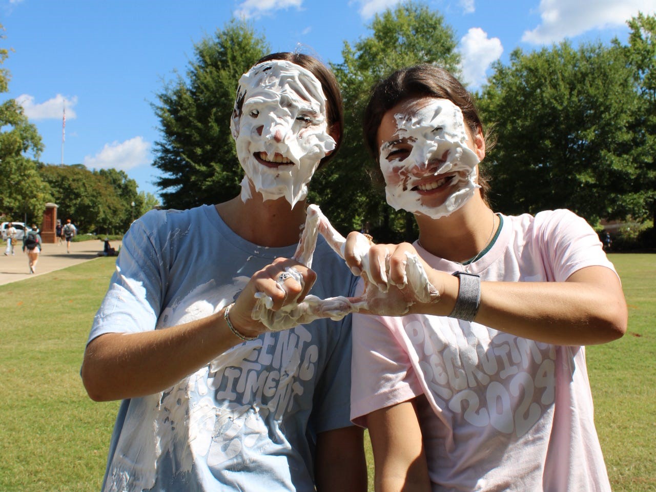 Two women with shaving cream on their face holding up the Tri Delta hand sign.