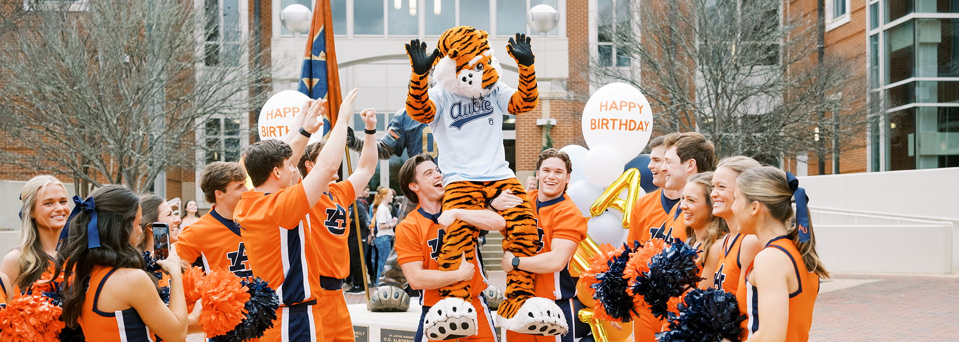 cheerleaders hoist Aubie on their shoulders in front of the student center during Aubie's Birthday celebration
