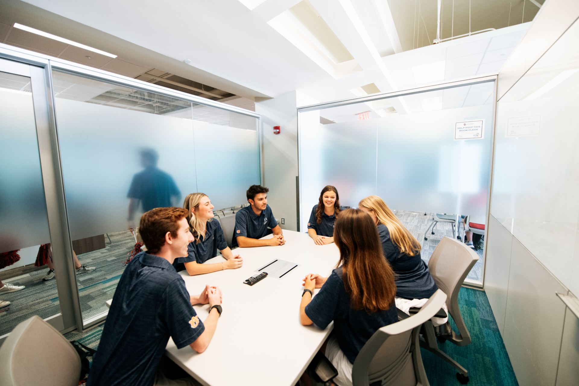 Students seated around a rectangular table in a room with glass walls
