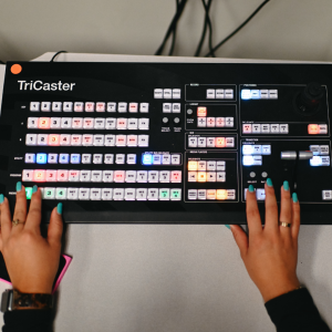 A student's hands using a tricaster video switcher