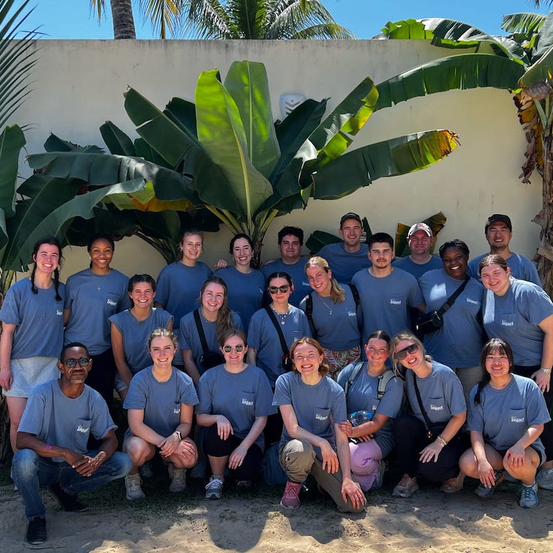 group of students posing in front of a wall with palm trees