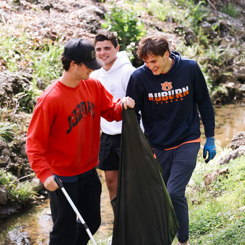 Three students picking up trash on a creek bank