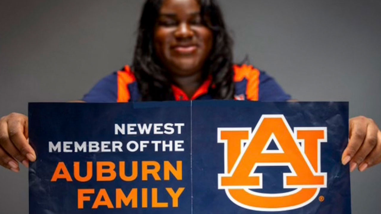 An Auburn student holding a brochure that says Newest member of the Auburn Family