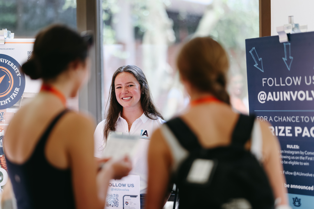 an involvement ambassador smiling at two other students who are looking at banners beside her