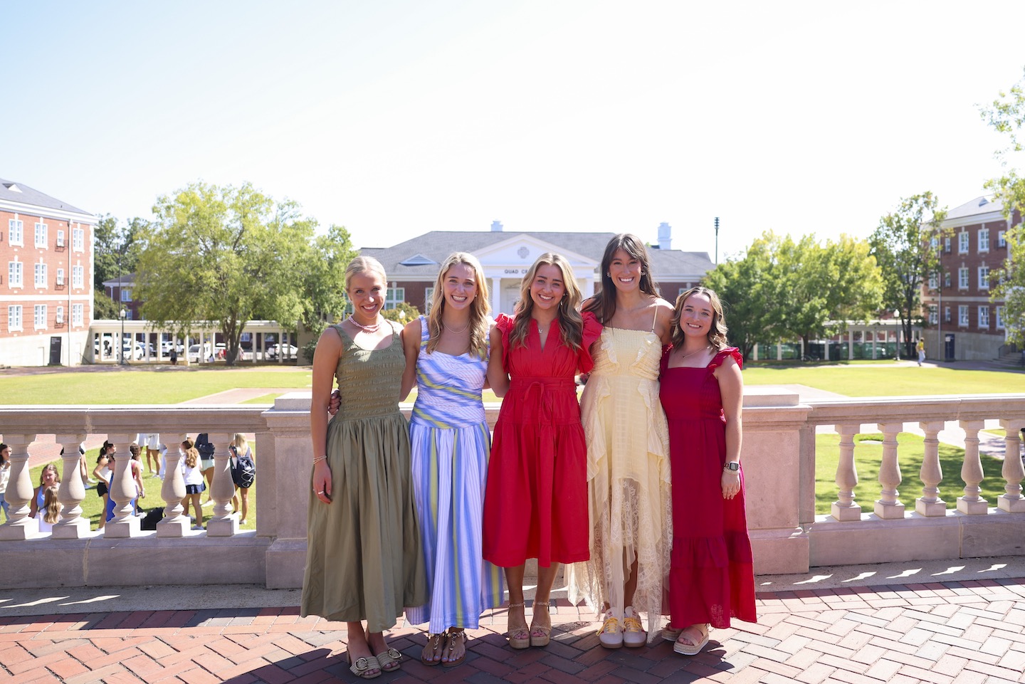 Five Auburn Miss Homecoming candidates pose together outside with dorms and the Quad Center in the background