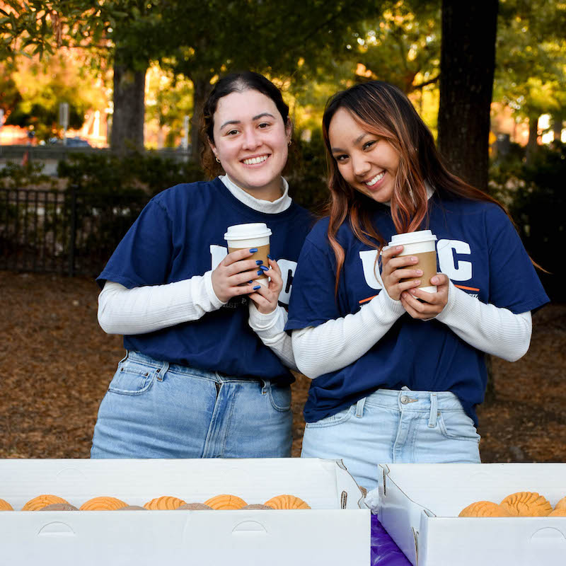 Two students posing for a photo at a table with cupcakes on it