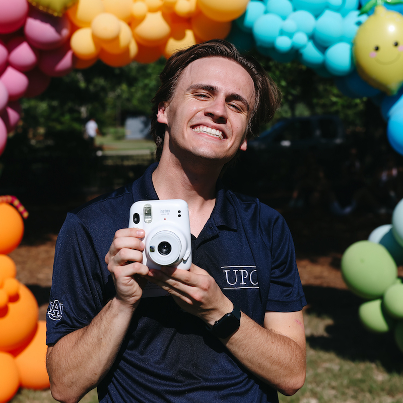 A student in a UPC shirt holding an instax camera to take a photo