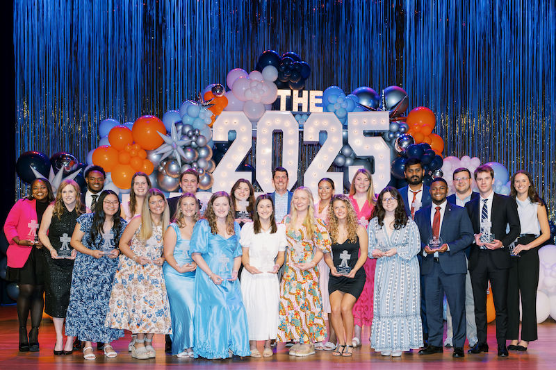 two students posing with an award on stage in front of the Involvement Awards sign