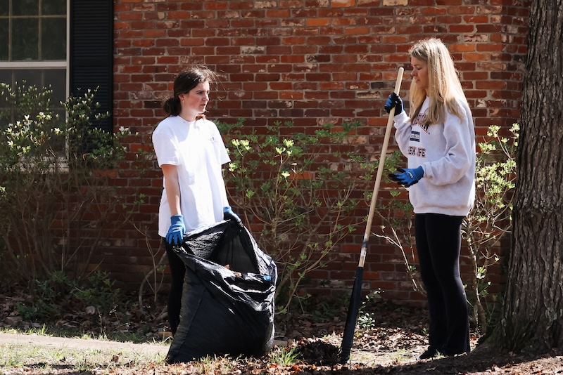 Two students raking leaves in a yard