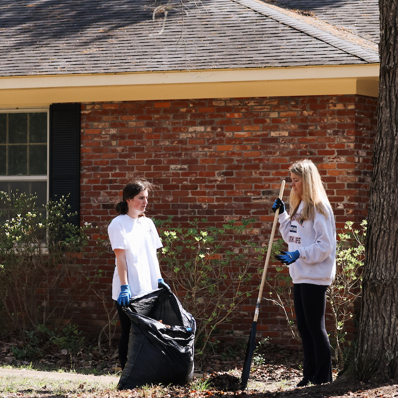 Two students raking leaves in a yard
