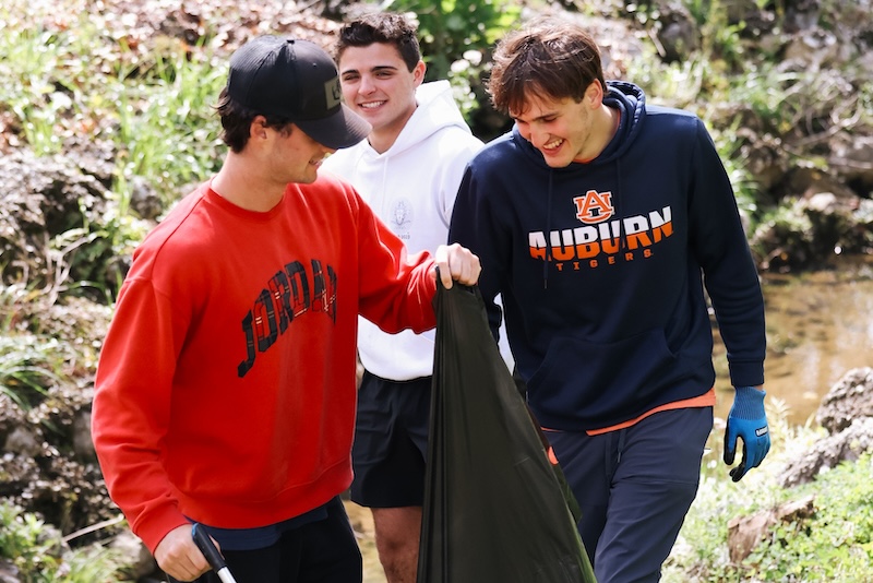 Three students picking up trash on a creek bank