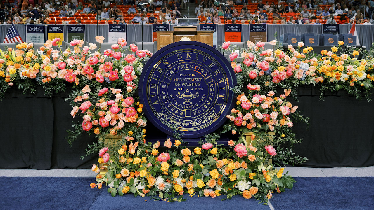 The Auburn University Seal in from of the podium at commencement surrounded by flowers.
